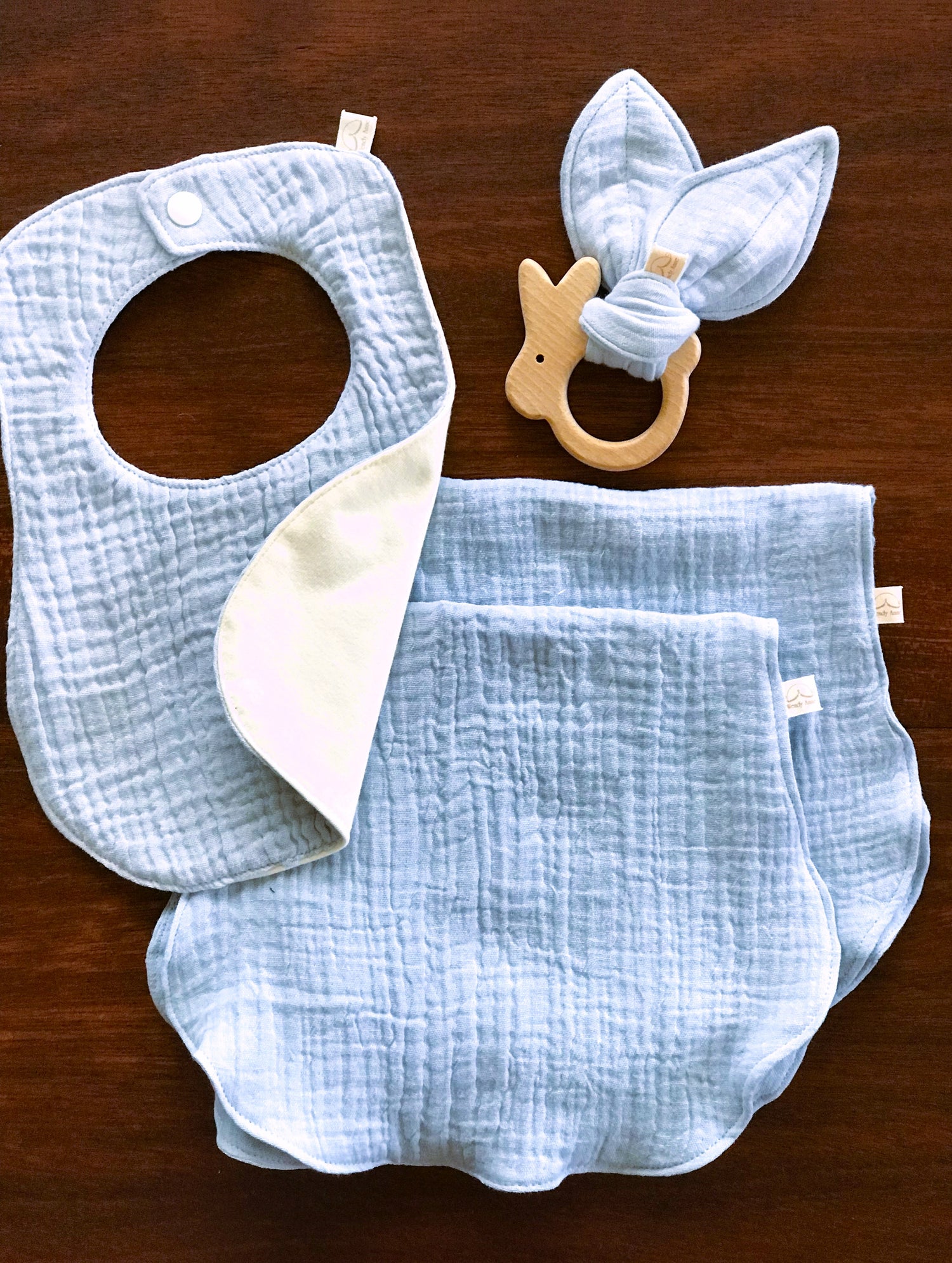 baby blue bib with waterproof backing, bunny beech wood teether with matching bunny ear fabric, 2 matching baby blue organic cotton burp cloths 