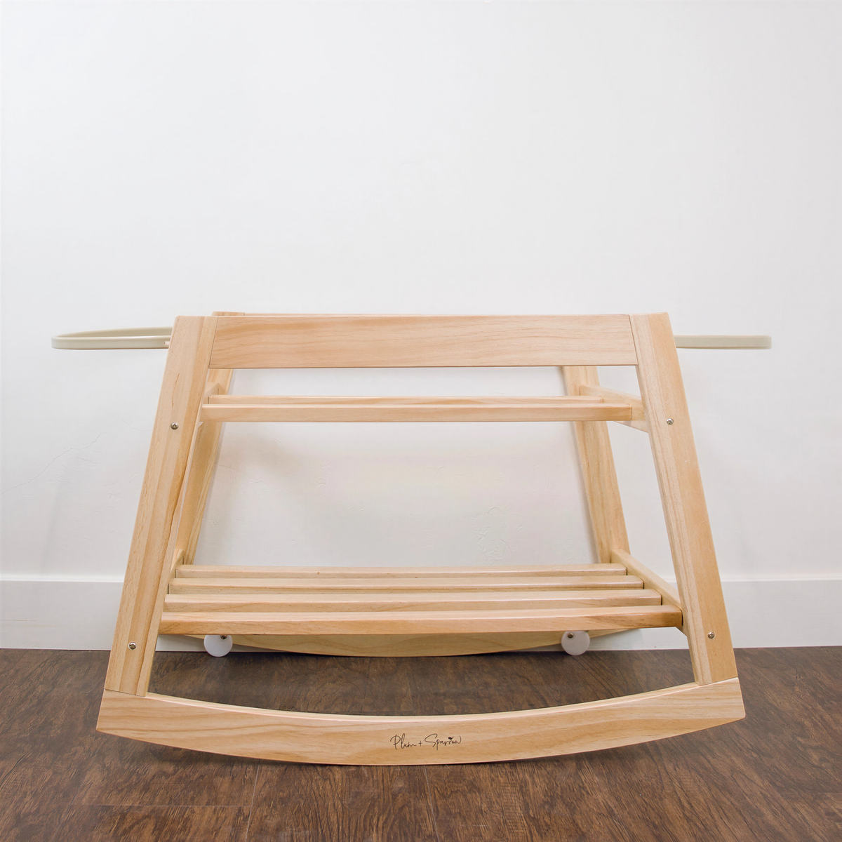 A wooden rocking chair with a curved backrest and footrests, positioned on a wooden floor against a white wall.