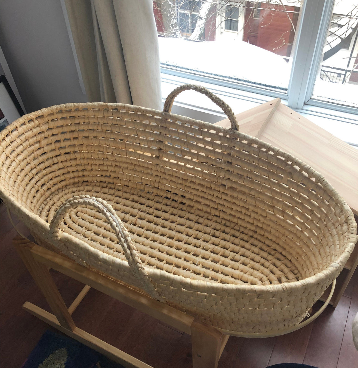 A woven basket with handles, placed on a wooden stand near a window.
