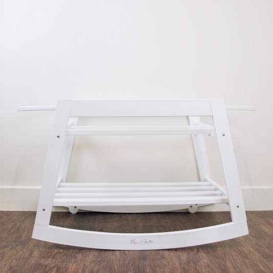 A white wooden rocking chair with a shelf underneath, placed on a wooden floor against a white wall.