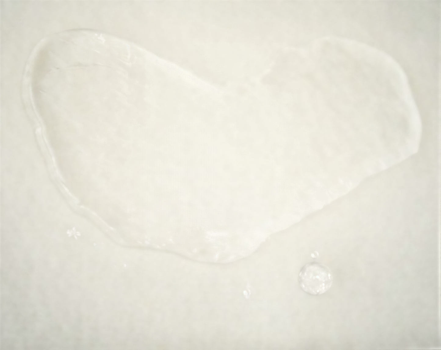 a single drop of water on a white surface, with a small circular object near it.