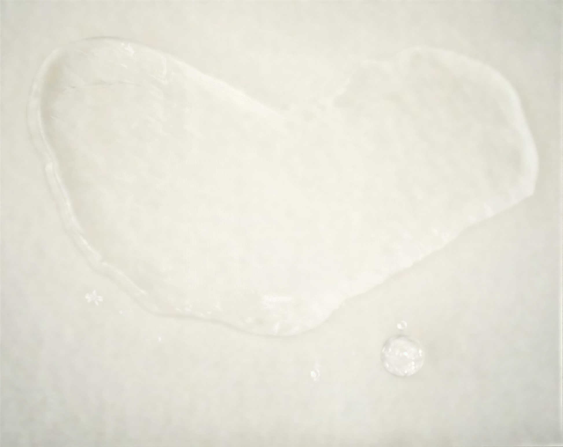 a single drop of water on a white surface, with a small circular object near it.