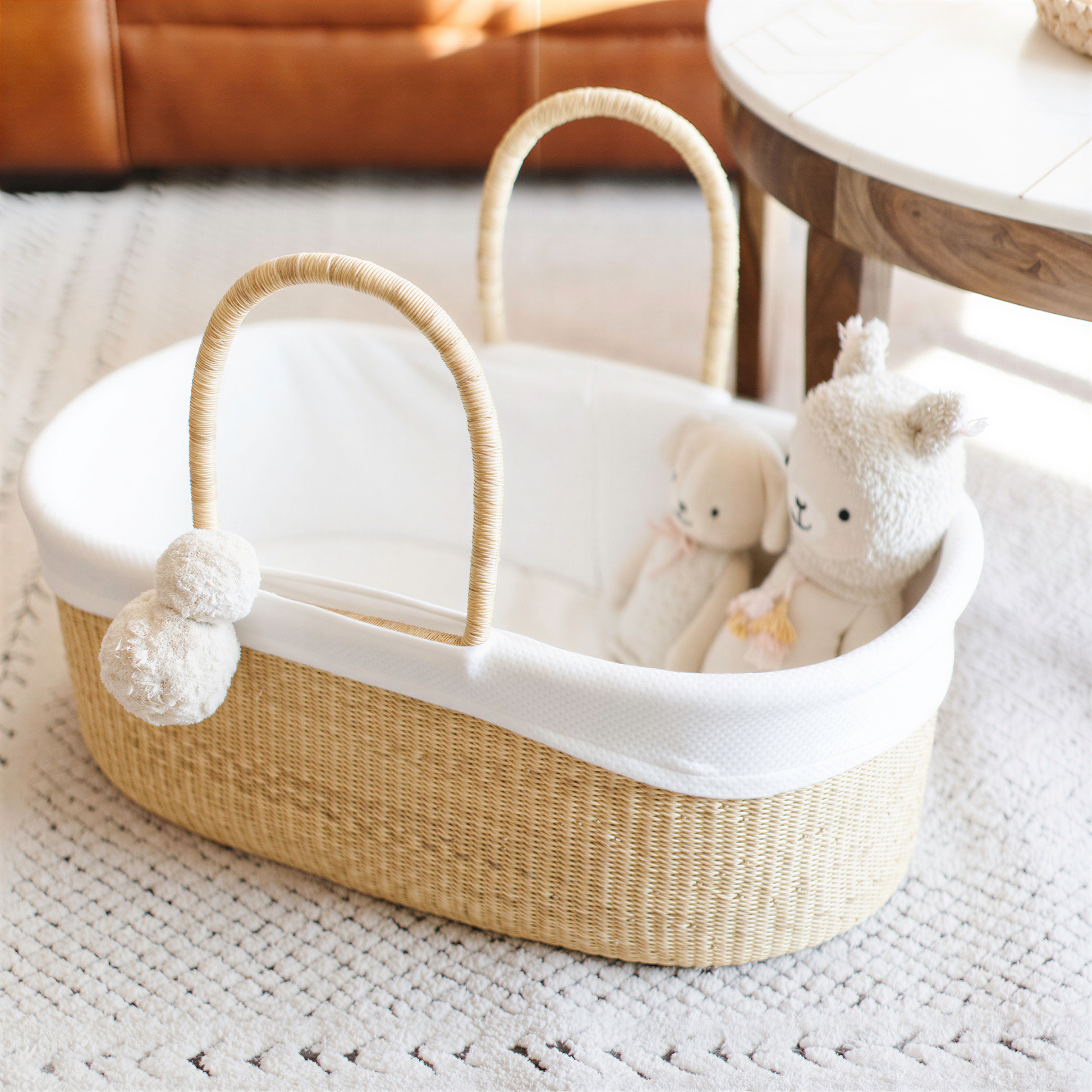 A woven basket with a white interior and handles, containing two stuffed animals and a white stuffed lamb.